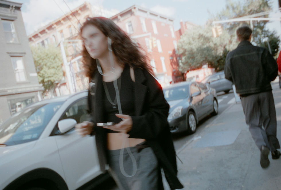 Person with long wavy hair walks on city street holding phone.