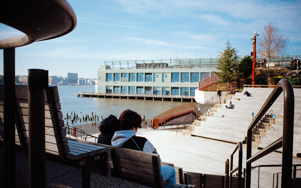 People sitting by waterfront building under blue sky.