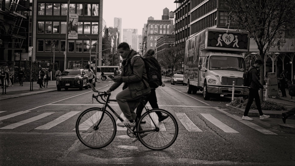 Man on bicycle checks phone while crossing busy city street.