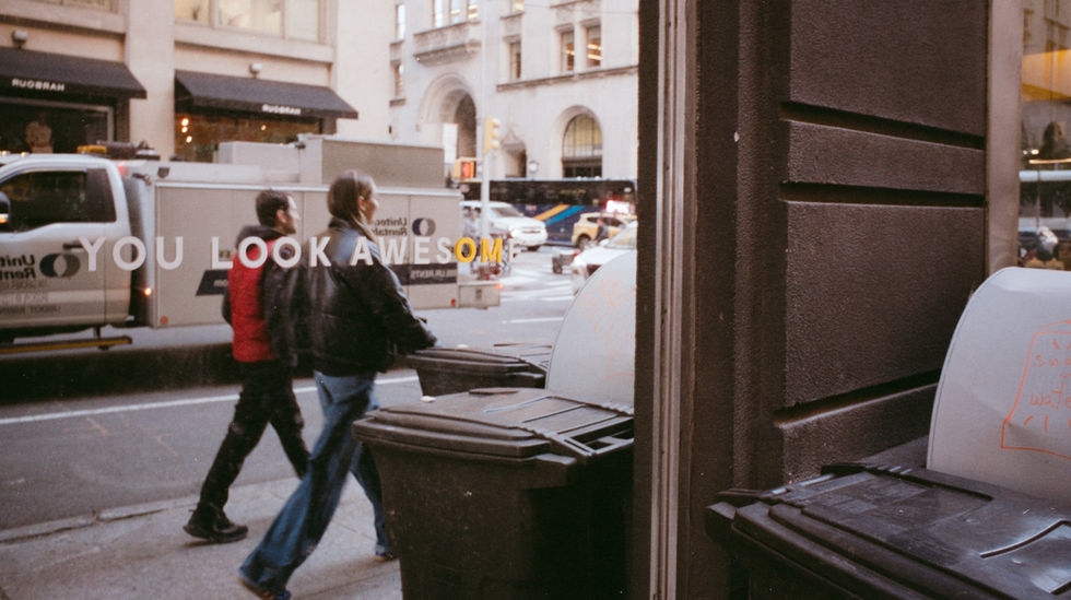 Two people walk past window with "LOOK AWESOME" text, city street.