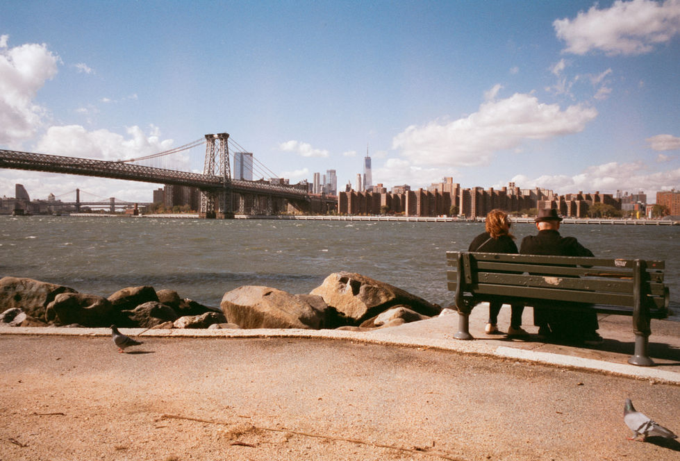 Couple on bench overlooking Williamsburg Bridge and New York City skyline.