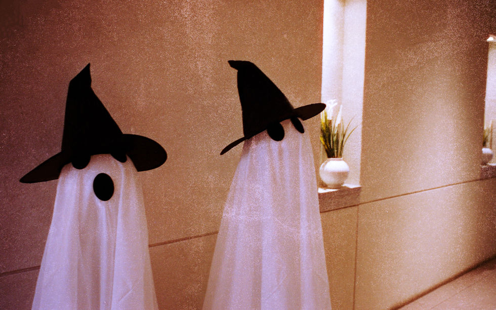Two ghost figures wearing black witch hats indoors.