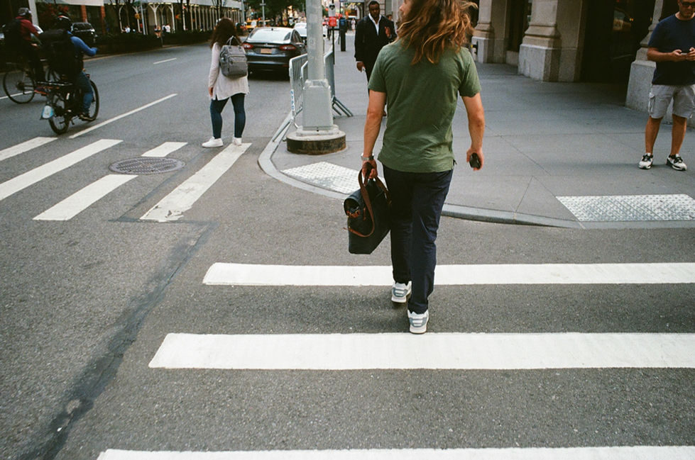 Person with long hair walking across city crosswalk carrying a bag.