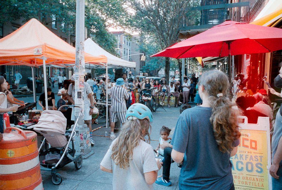 Outdoor street market scene with many people, colorful tents and umbrellas.