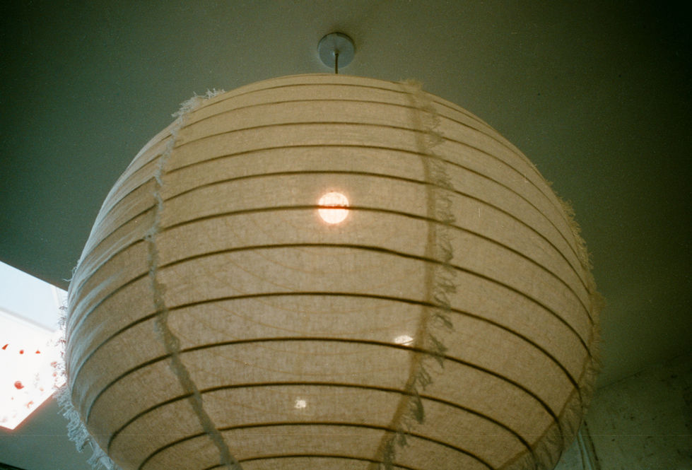 Round paper lantern light fixture hanging from ceiling with glowing bulb inside.