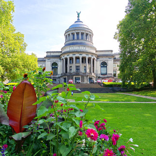 un beau bâtiment dans le parc du Cinquantenaire avec des fleurs au premier plan