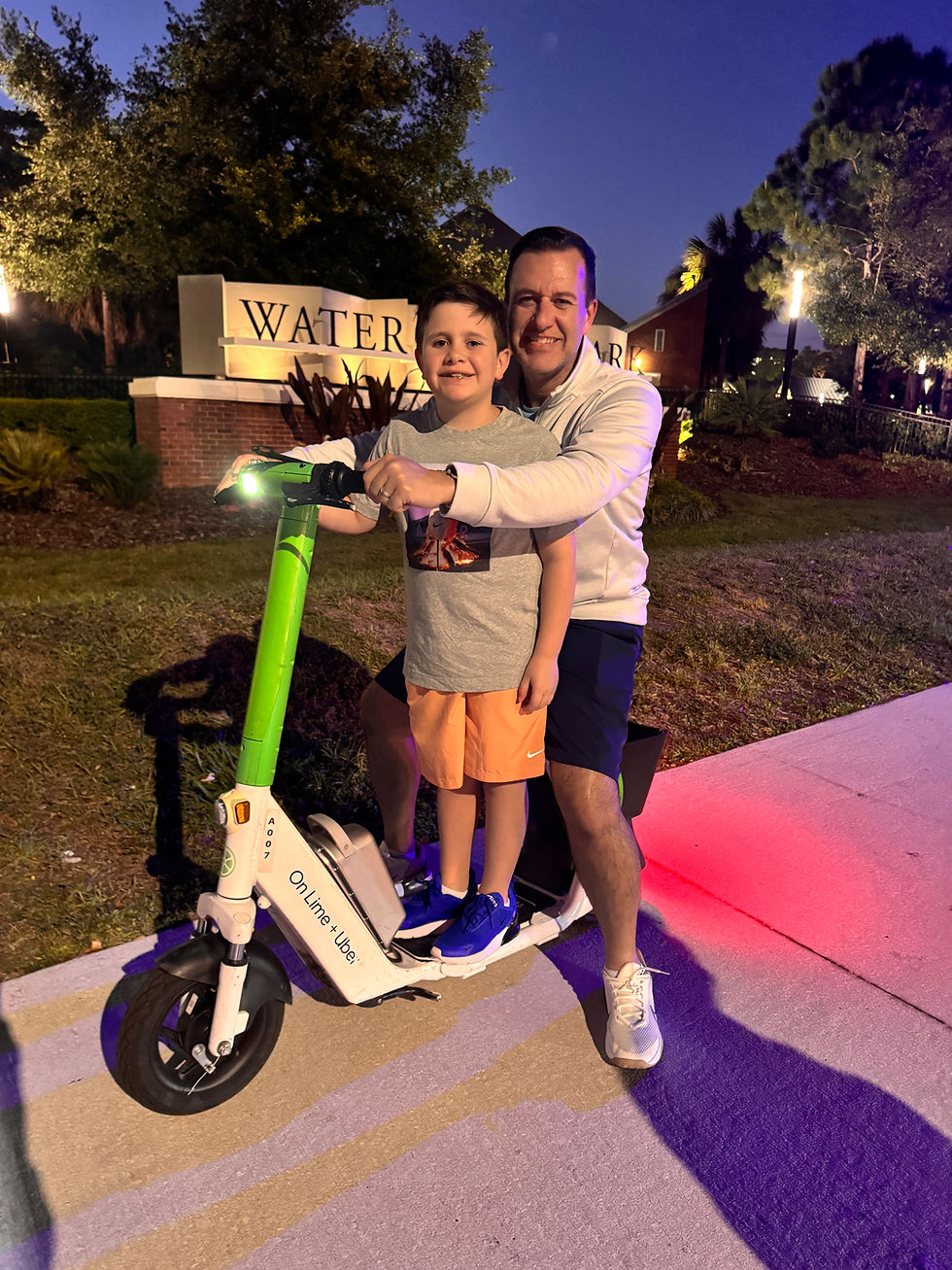 A man and child on an e-scooter at dusk, smiling. Sign reads "Water". Bright green handles, text "On Lime + Uber". Trees in the background.