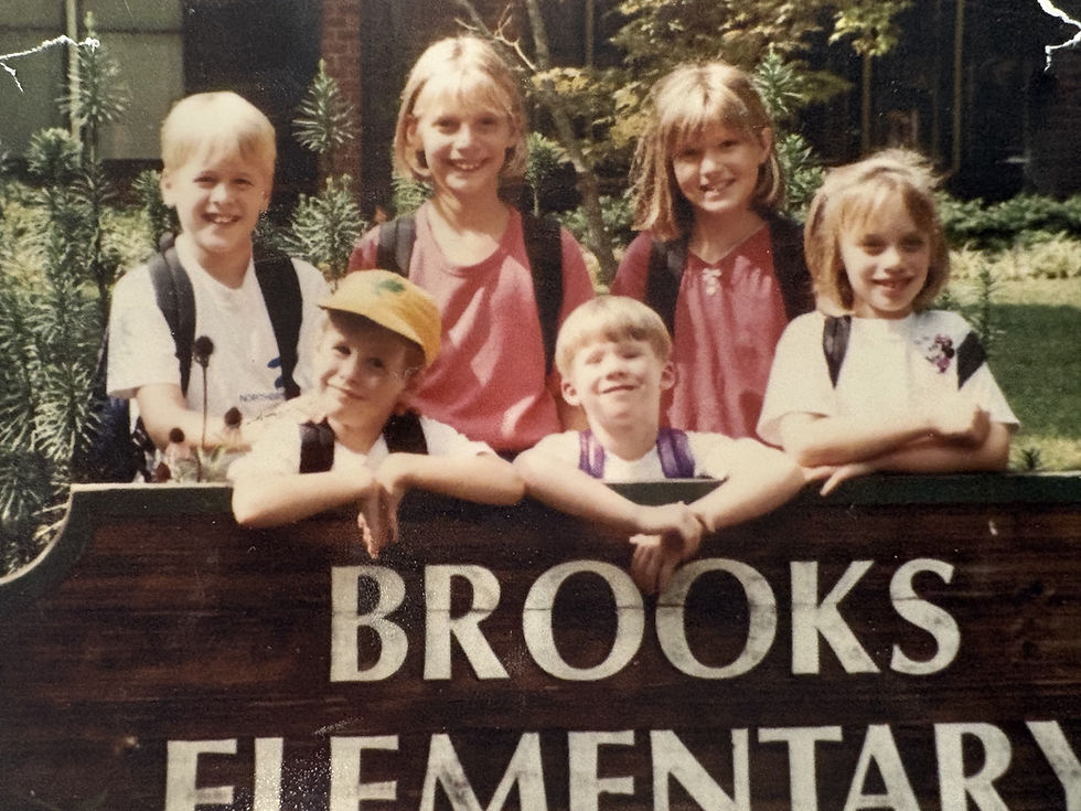A photo of children by the Brooks Elementary Sign, including 4th grade teacher Breck Brown