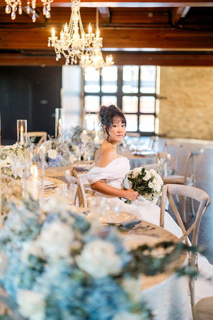 Bride sitting at a formal table setting draped in blue and white flowers