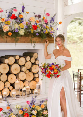A bride holding a colorful bouquet and standing next to colorful floral arrangements