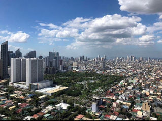 白くふわふわとした雲が浮かぶ明るい青空に向かって伸びる、洗練されたモダンな高層ビル群を下から見上げたアングル。