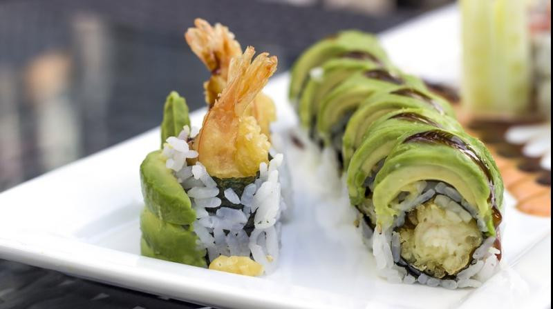 sushi up close perfectly arranged with prawn tails sticking out and rings of green avocado