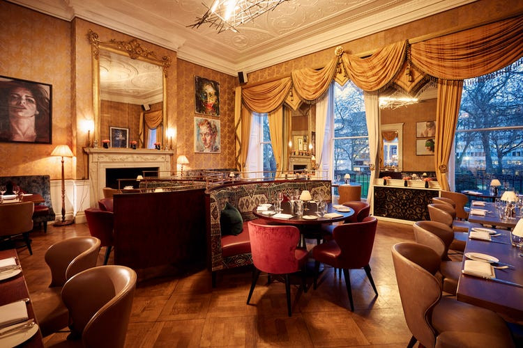 A drawing room in Home house members club in Fitzrovia, with seating and tables and big curtains by the window