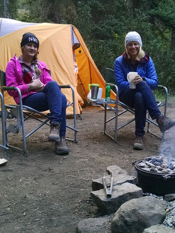 Campers on a backcountry pack trip sit by the fire, coffee in hand, waiting for a Dutch oven breakfast!