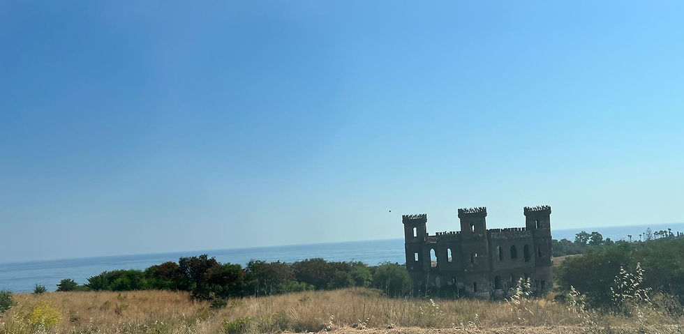 A picture of an abandoned castle in a golden field with the Mediterranean Sea in the background.