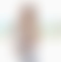 Pregnant woman in white tank top touches her belly, standing outdoors with ocean and greenery in the background. Bright, serene mood. Pregnant travel insurance