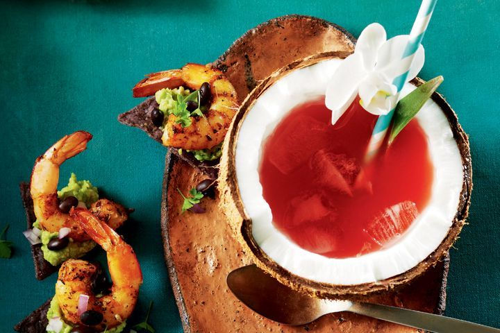 Coco loco cocktail in half a coconut, with shrimps on the side, pineapple leaves and a white flower