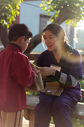 STL volunteer, sitting down, gives a brown paper bag to a young male child.