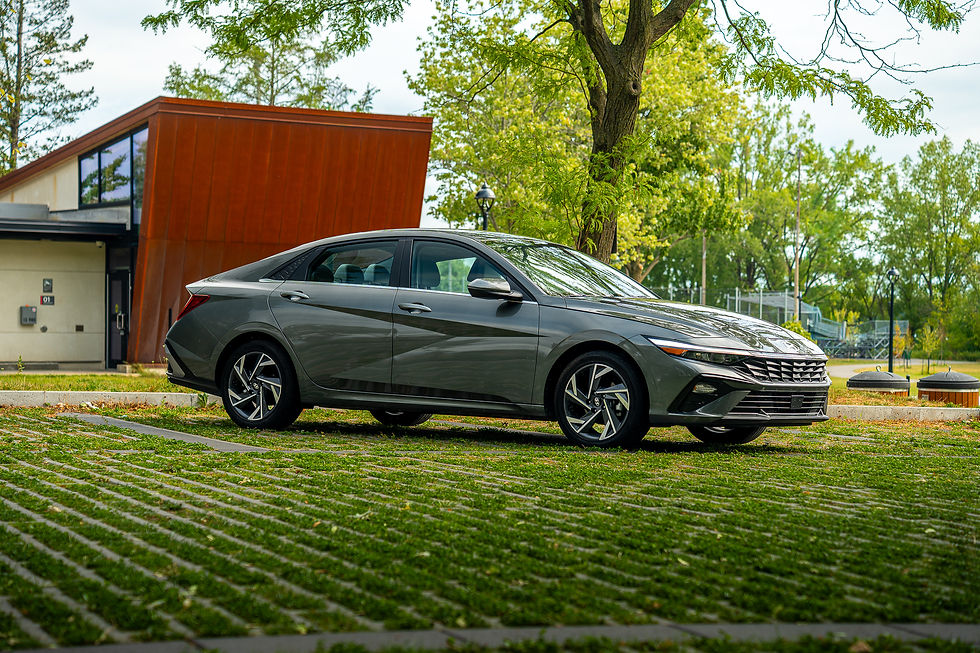 Hyundai Elantra Hybrid - Gray car parked on grass near a modern building, with trees and a clear sky in the background. Mood is calm and serene.