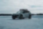 2026 Volvo EX30 Cross Country -Silver SUV with roof rack on snowy terrain, cloudy sky, distant treeline. Mood is serene and chilly.