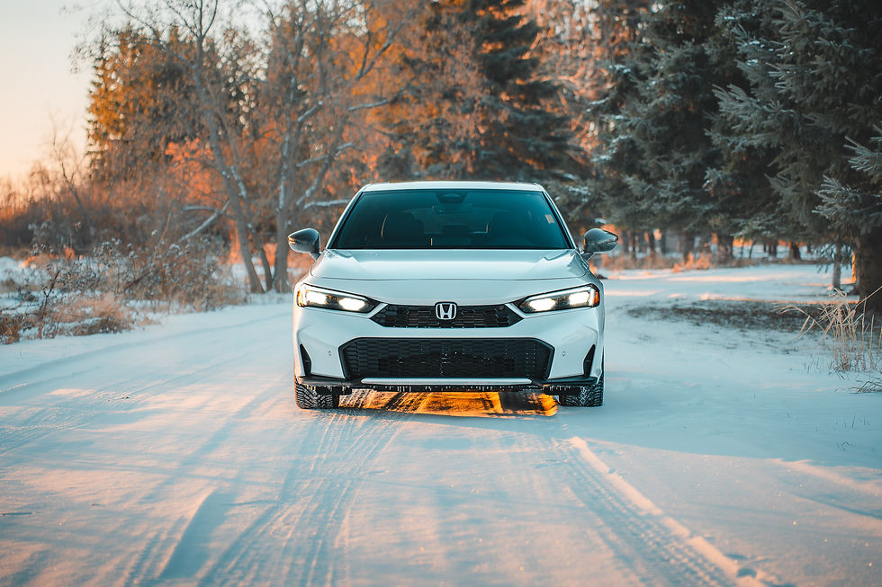 2026 Honda Civic Hybrid Hatchback White car on snowy road, surrounded by trees in golden winter light. The car's headlights are on, creating a warm glow on the snow.