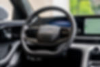 Omoda 9 - Close-up of a ŠKODA steering wheel and digital dashboard inside a modern car, with a glowing green navigation screen.