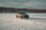 2026 Volvo EX 30 Cross Country - A Volvo SUV drives swiftly across a snowy landscape, with blurred motion showing speed. Snow-covered ground and distant forest in background.
