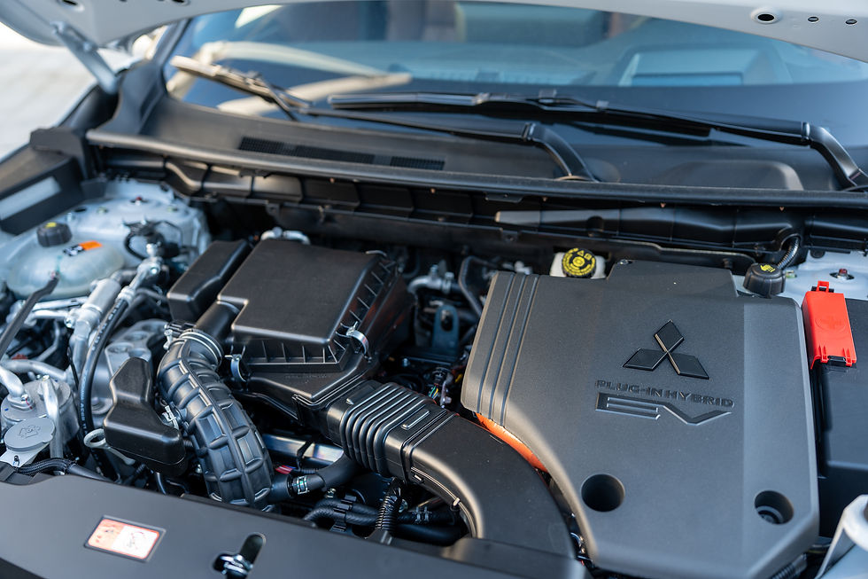 2026 Mitsubishi Outlander PHEV - Car engine with a Mitsubishi logo and "Plug-In Hybrid EV" text. Visible black and silver components under an open hood, well-lit setting.