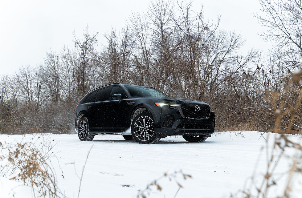 Black Mazda CX-70 PHEV SUV on a snowy road, surrounded by bare trees and power lines. Overcast sky, capturing a wintery, calm atmosphere.