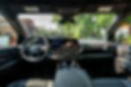 Dashboard view of a Chevrolet Silverado EV truck interior with a digital display, steering wheel, and two cans on the console. Trees visible outside.