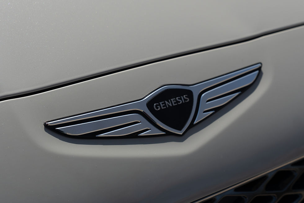 Close-up of a metallic Genesis car emblem on a gray surface, featuring a winged design against a sleek, shiny background.
