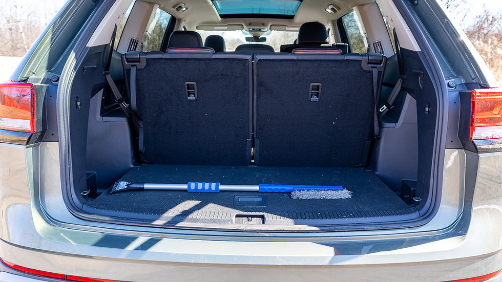 Open VW Atlas trunk with a folded rear seat, showing a blue snow brush inside. The car is parked outdoors on a sunny day.