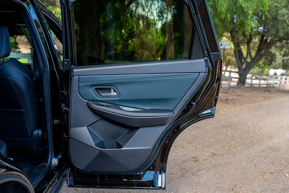 2027 Nissan Rogue E-power SR - Open black SUV rear door with blue-gray panel, parked on a dirt road with trees and fence in the background.