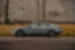 Hyundai Sonata parked on a road with overgrown grass and a stone wall in the background. Overcast atmosphere.