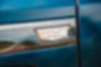 Close-up of a shiny Cadillac emblem on a metallic blue vehicle. The angular badge is set against a smooth, reflective surface.