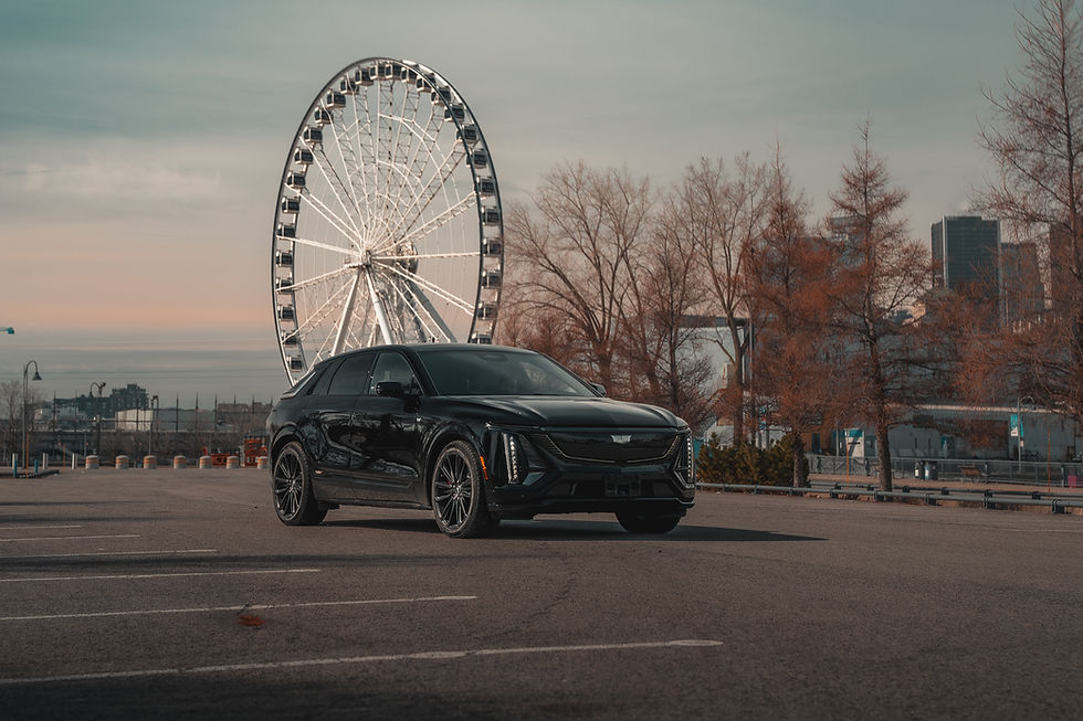 2026 Cadillac Lyriq-V - A black car is parked in an empty lot with a Ferris wheel and city skyline in the background. The scene is calm with bare trees around.