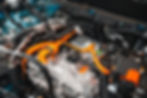 Close-up of a Cadillac Vistiq car engine with bright orange and black cables. Metallic components and labels are visible. Detailed and technical.