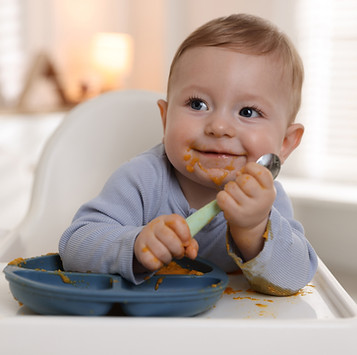 Cute little baby eating healthy food in high chair indoors.jpg