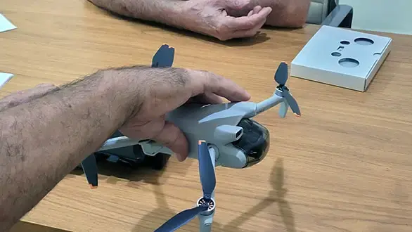 Detalhe da mão de um instrutor da Escola de Drone Santa Catarina segurando um mini drone cinza com as hélices dobradas, mostrando sua portabilidade e design compacto.