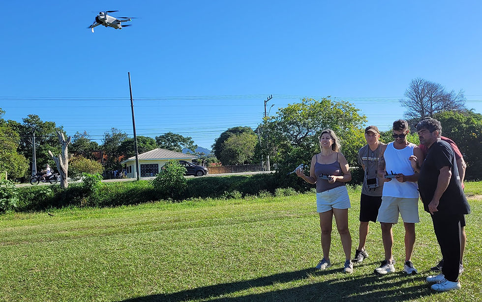 Grupo de alunos opera drone DJI  em campo gramado sob céu azul em Florianópolis SC, com casas e árvores ao fundo na aula da Escola de Drone Santa Catarina.