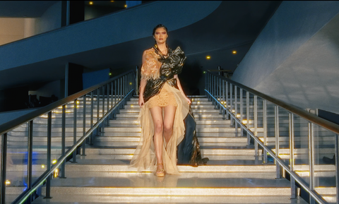 Runway model walking down exterior staircase in gold gown – Raised Media Co