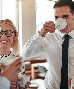 Zwei glückliche Mitarbeitende im Büro bereiten gemeinsam Kaffee zu und lachen miteinander | noury.ch