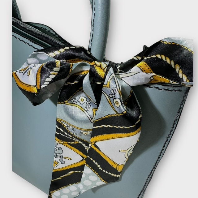 Thumbnail: The close up scarf view of a dusty blue leather Italian satchel bag with patterned silk scarf tied in a bow.