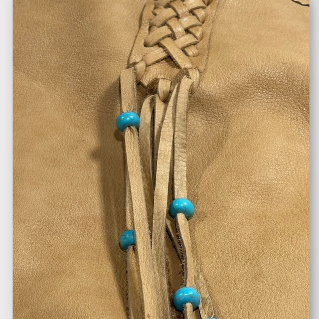 Thumbnail: The close up view of a deerskin leather shoulder bag with turquoise howlite beads and braided deerskin accents..