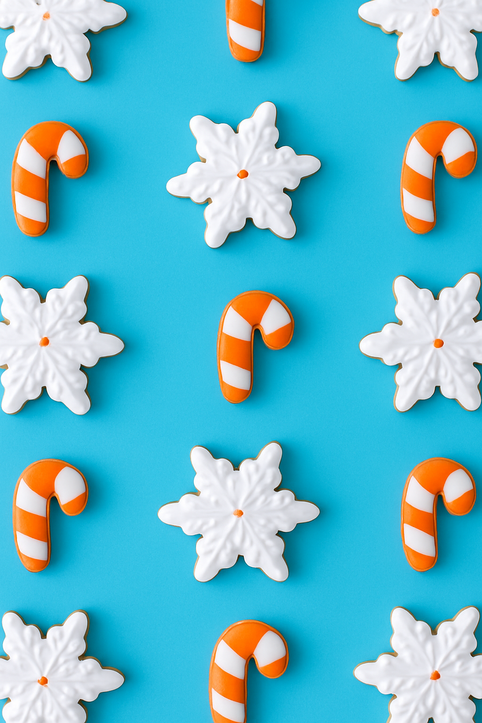 white snowflake cookies and white and orange candy cane cookies on a blue background