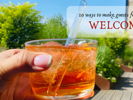 A hand holding a bright orange summer drink outdoors on a sunny patio with greenery in the background