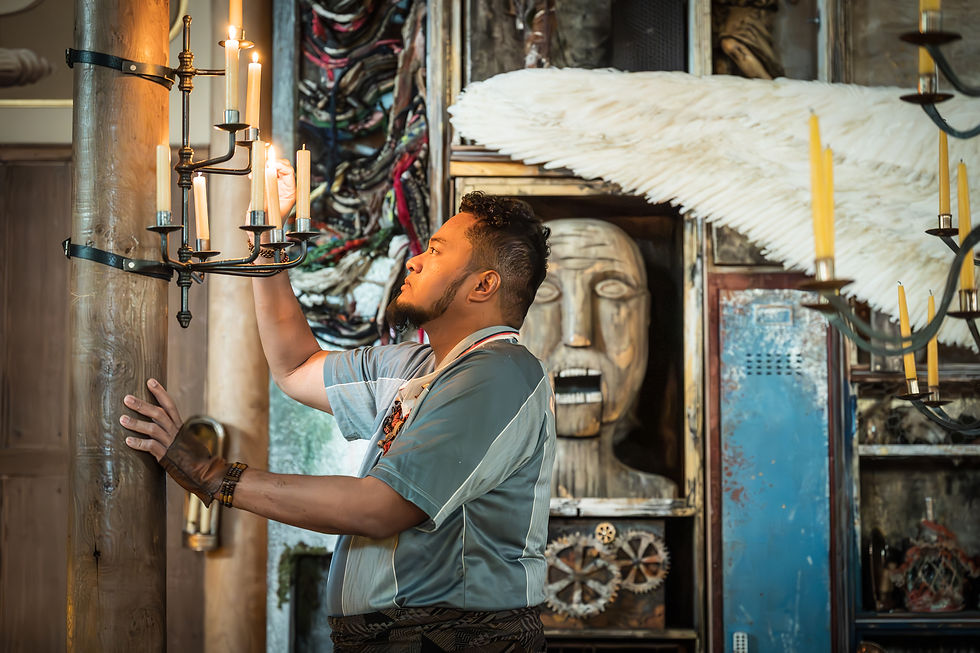 A man photographed standing in profile, he is touching some candles