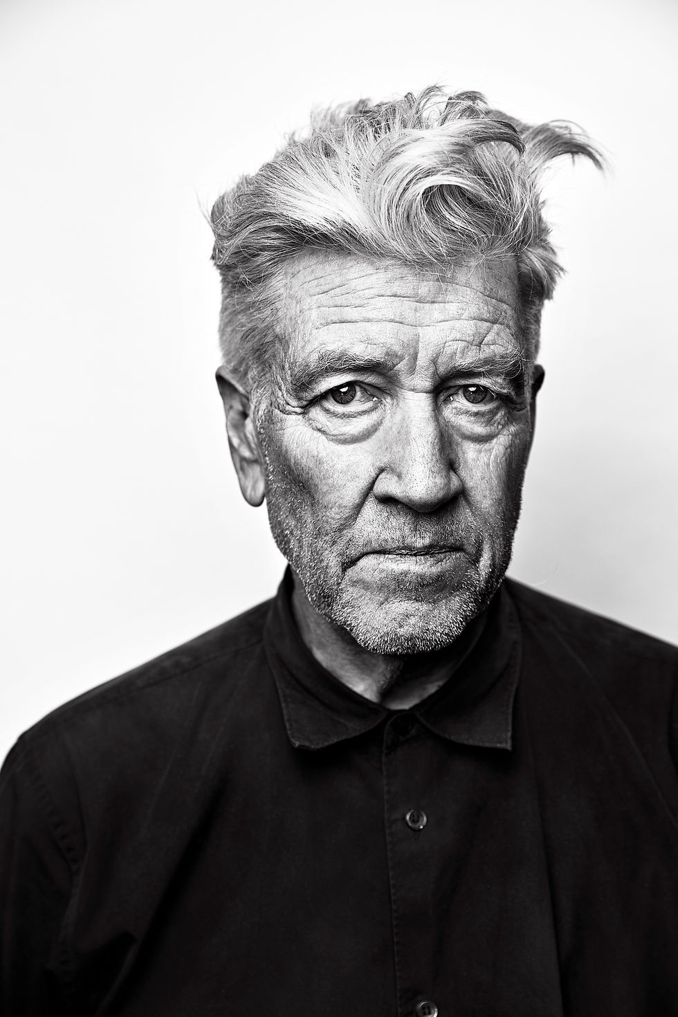 Black-and-white portrait of an older man with tousled gray hair and a stern expression against a plain white background