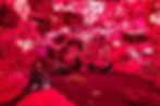People seated on a pink carpet with a canopy above resembling the inside of a heart