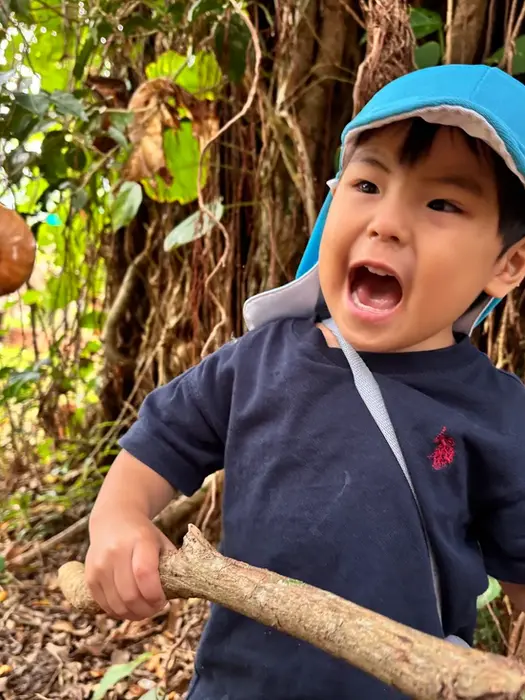 青い帽子の男の子が棒を持ち、カタツムリを見て興奮して驚いている